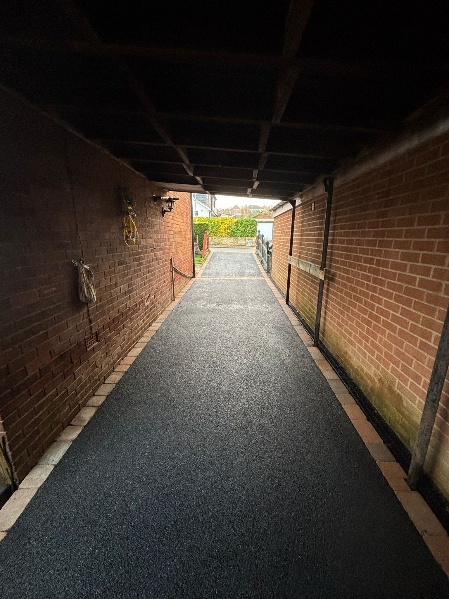 Covered brick walkway leading to a bright garden exit, with gravel path and brick walls on both sides