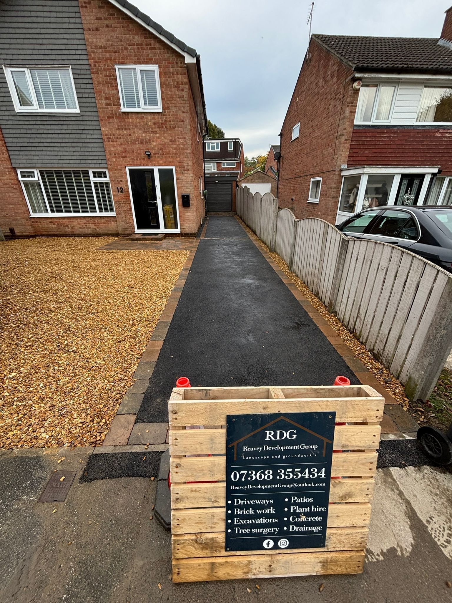 Driveway between brick houses with a wooden sign at the front and gravel on the left.