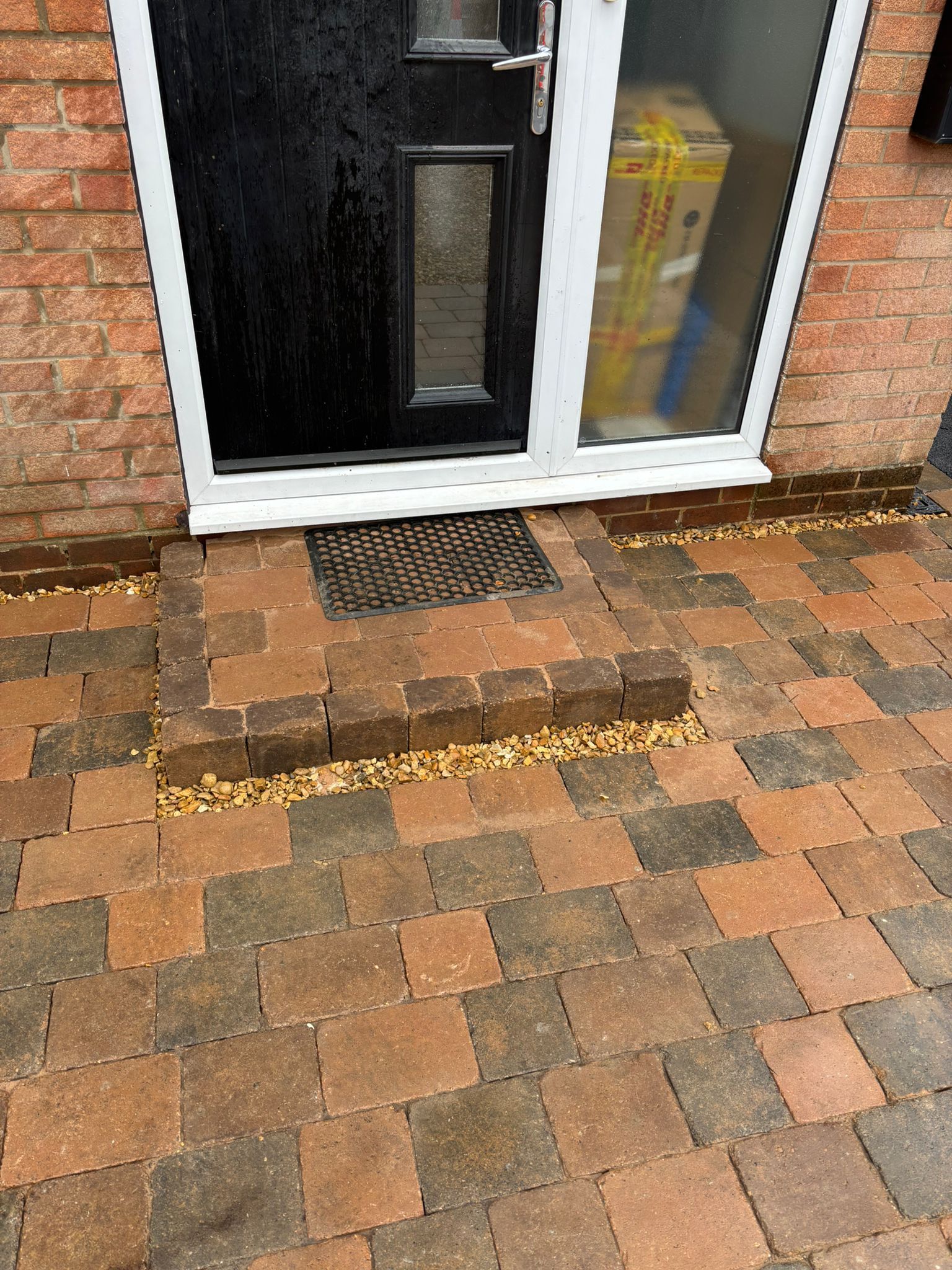 Front door with tiled step and wet brick driveway in front of a house