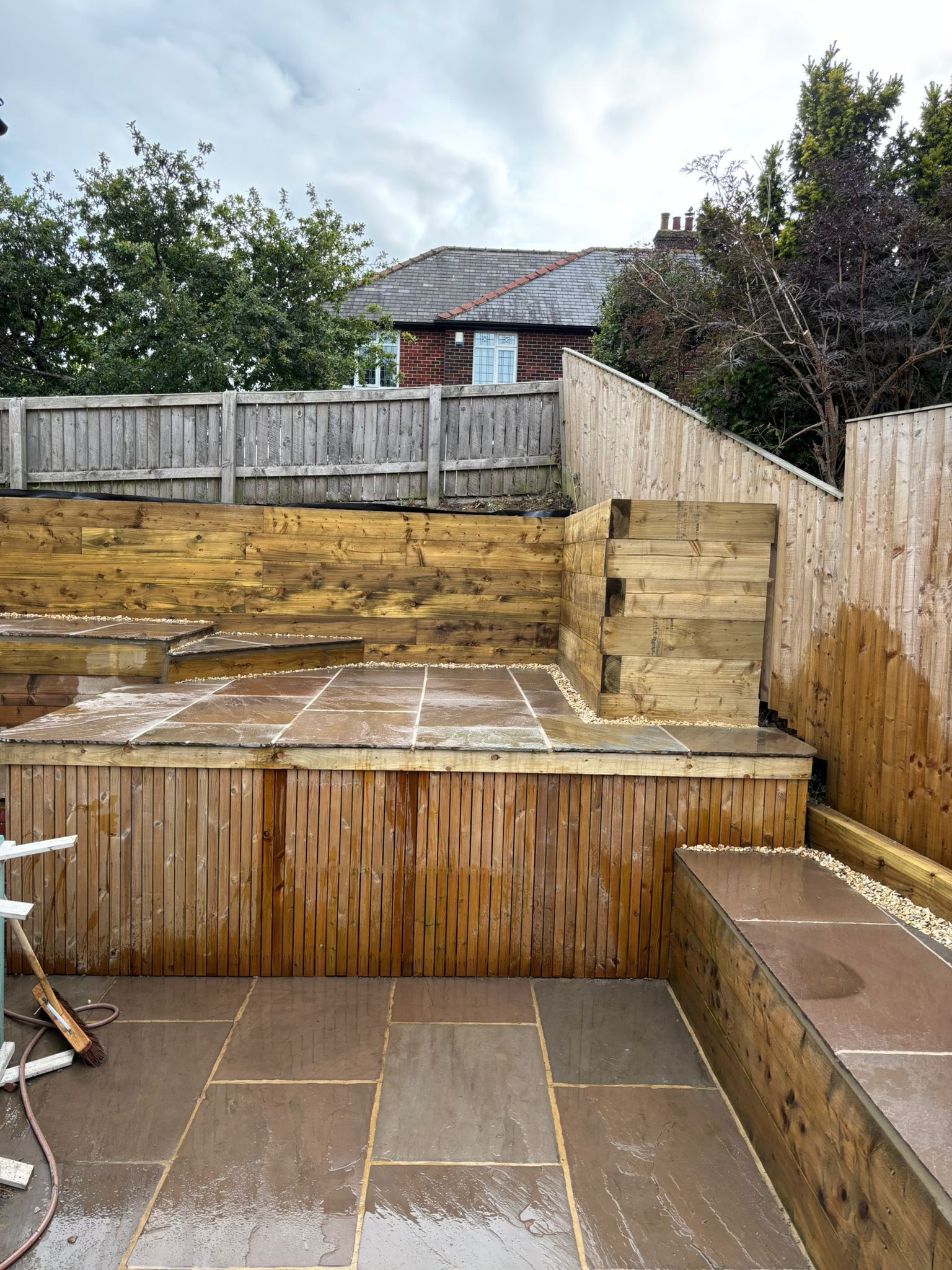 Backyard patio with raised timber deck, steps, and weathered fence under cloudy sky