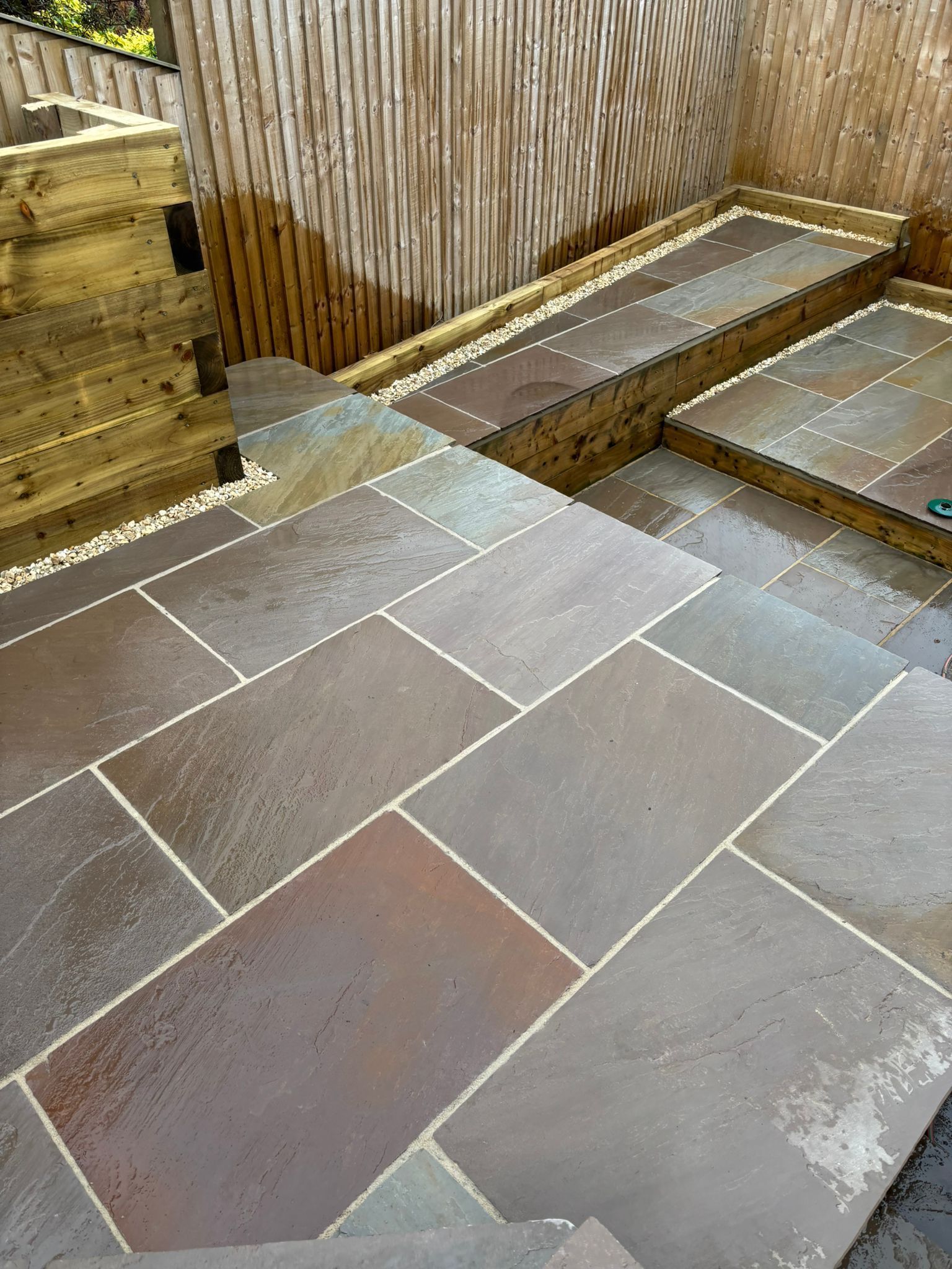 Stone patio steps beside a wooden fence, with wet slate tiles and a small water runoff channel