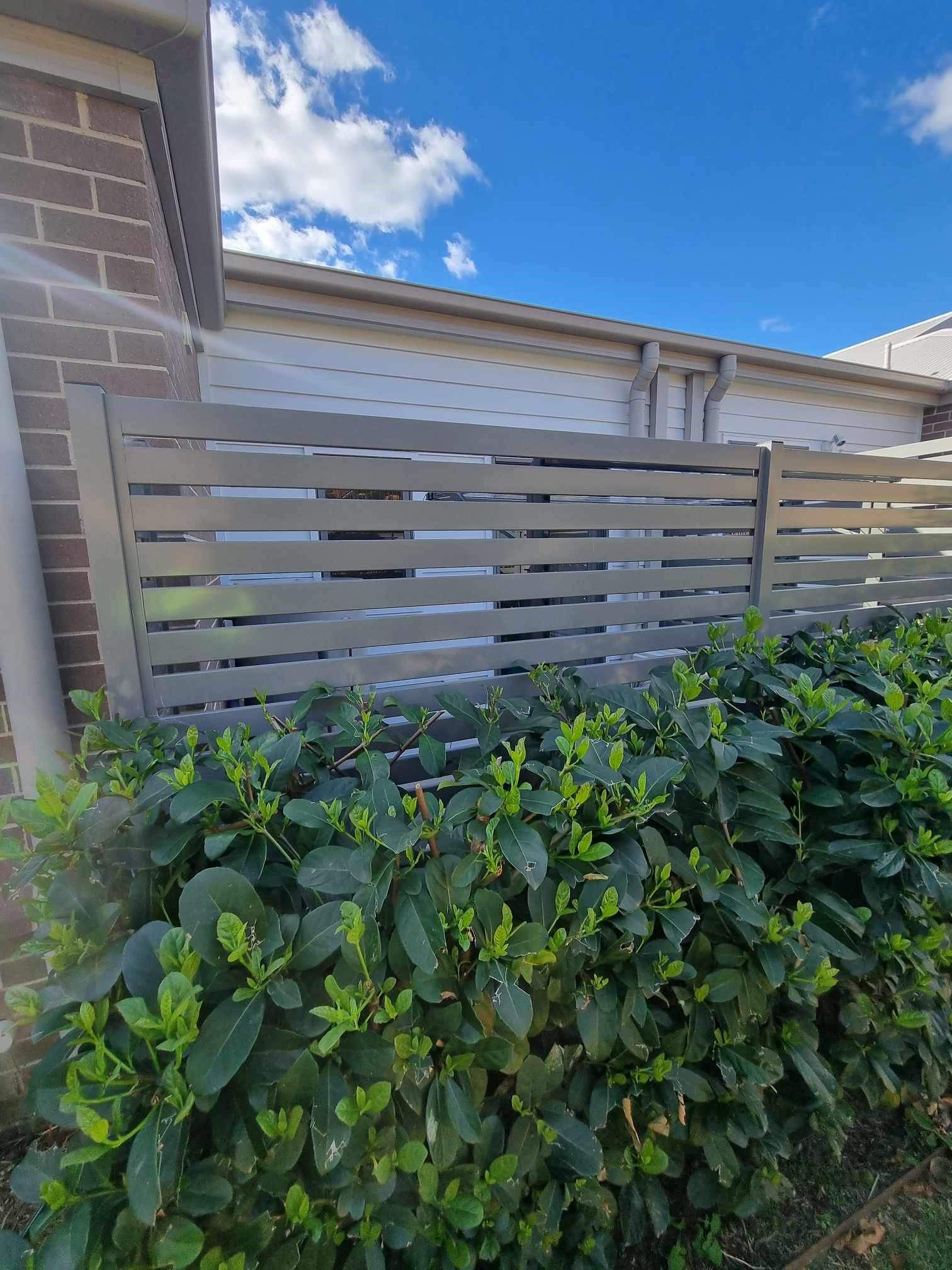 Grey slatted fence behind green leafy shrubs — D & T Balustrade Systems In Unanderra, NSW