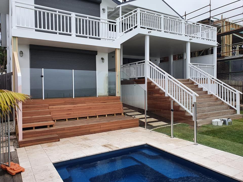 Two-story white house with wooden decks, stairs, and a pool in front — D & T Balustrade Systems In Unanderra, NSW