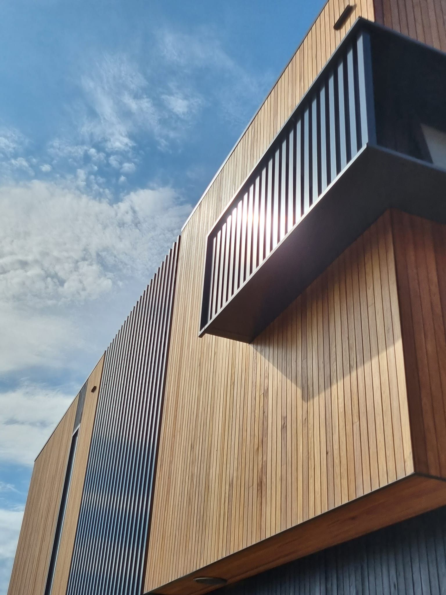 Modern building exterior with wood paneling and geometric lines against a cloudy blue sky — D & T Balustrade Systems In Unanderra, NSW