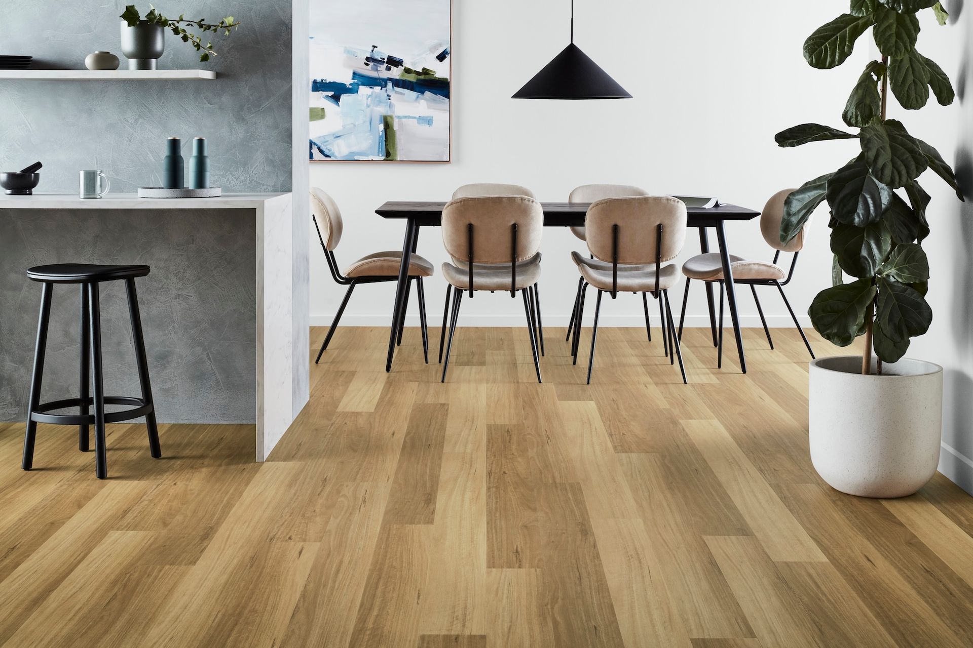 Dining room with wood floor, table, chairs, bar with stool, artwork, and potted plant.