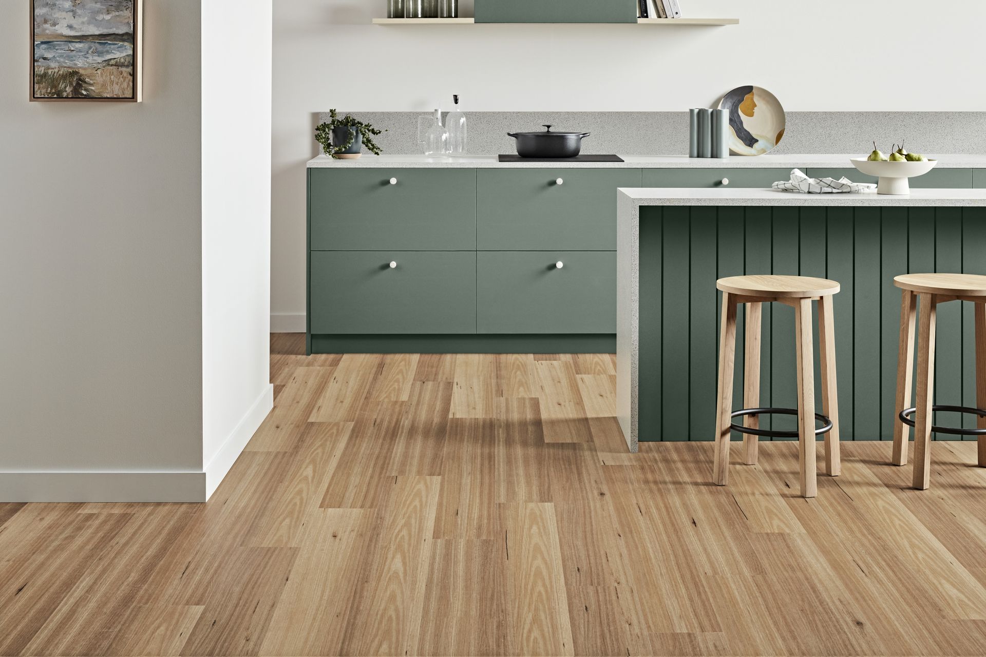 Wooden-floored kitchen with sage green cabinets, a white countertop, and bar stools.