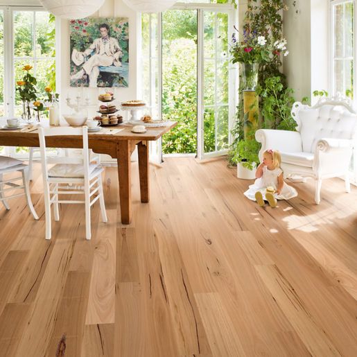Light wood flooring in a sunny room with a wooden table and chairs. A young child sits near a white chair.