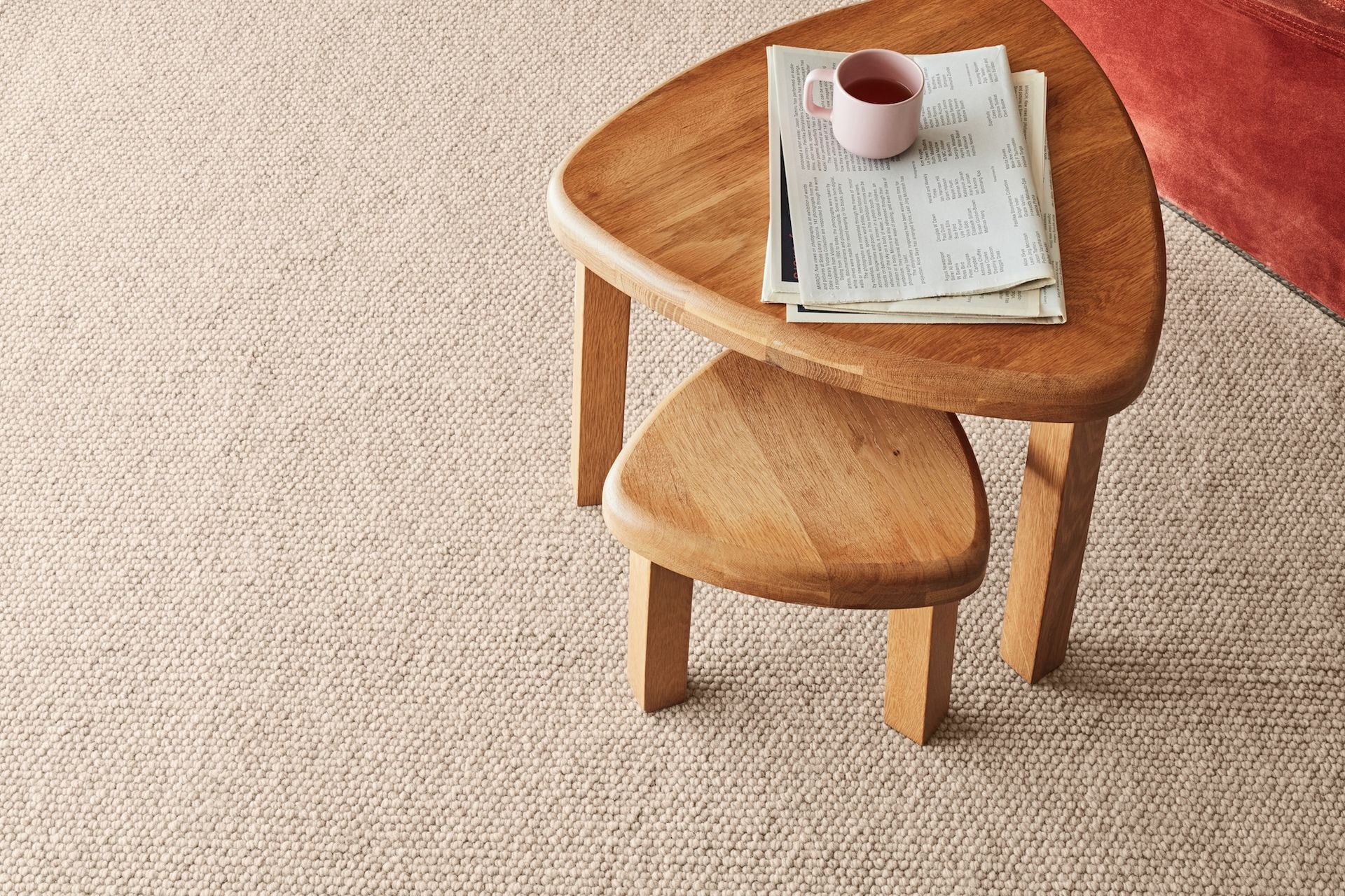 Wooden side table with newspaper and mug on textured beige carpet.