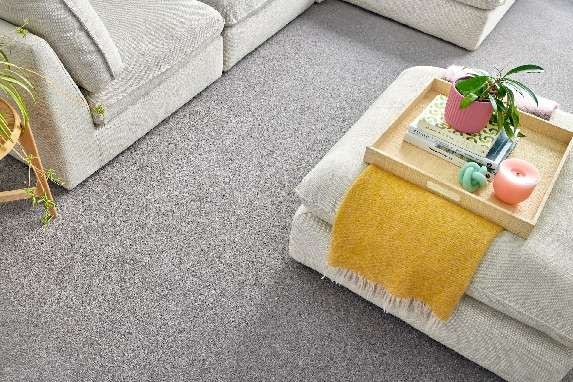 A cozy living room with gray carpet, a sectional sofa, and an ottoman with a tray holding a plant and candles.