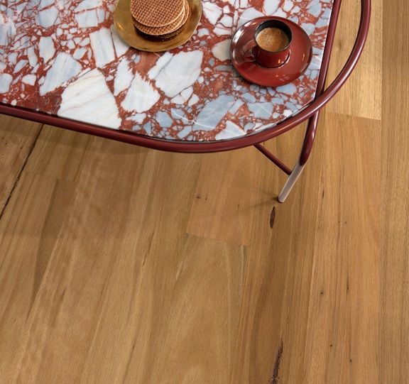 A table with a marble top holds a cup of coffee and cookies on a wooden floor.
