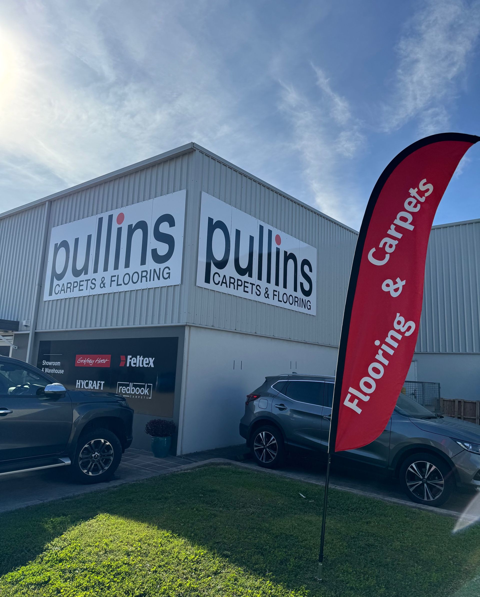 Pullins flooring store exterior with signage and a red flag advertising flooring and carpets. Cars are parked outside.