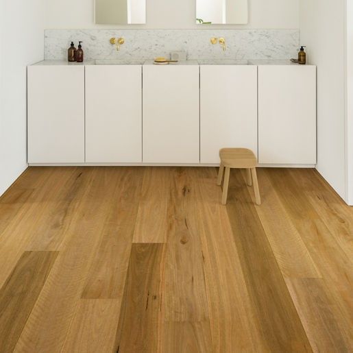 Bathroom with wood flooring, white cabinetry, and a wooden stool. A marble backsplash and mirrors are above the sinks.