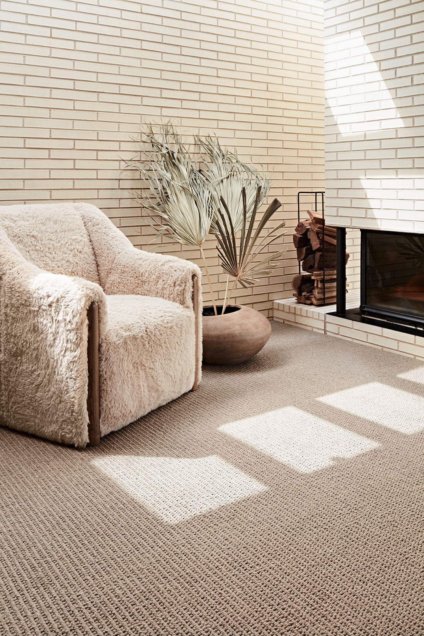 Cozy living room with a fluffy beige armchair, textured rug, and decorative items near a fireplace, bathed in sunlight.