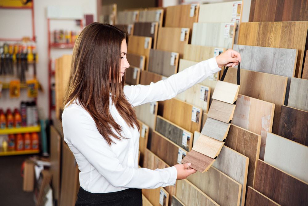 Woman in a white shirt examining wood flooring samples in a store.