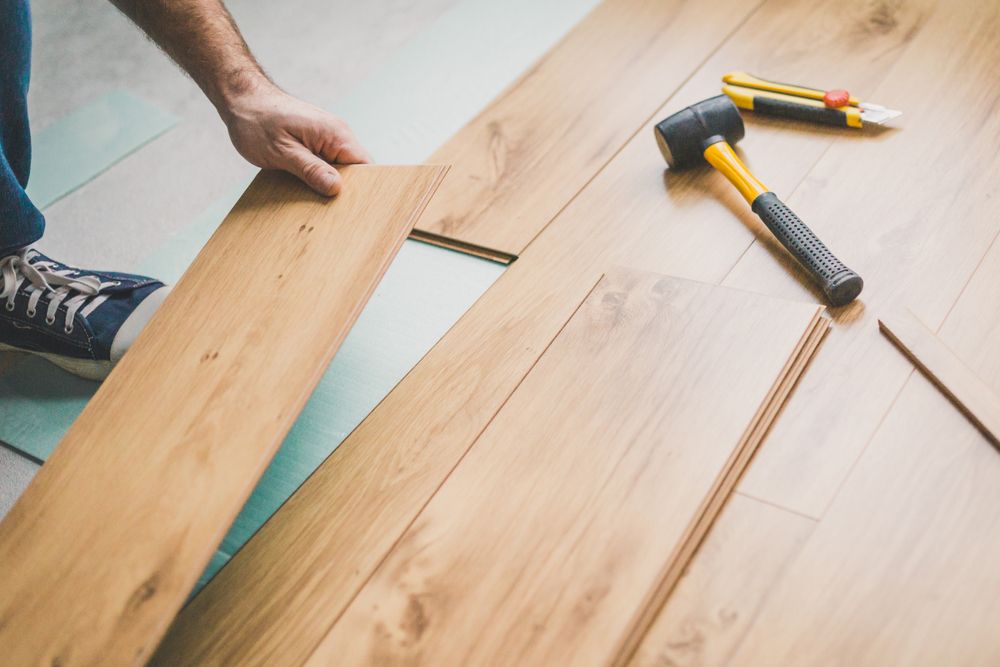 Person installing laminate flooring. Hands positioning a wood plank, with tools nearby on the floor.