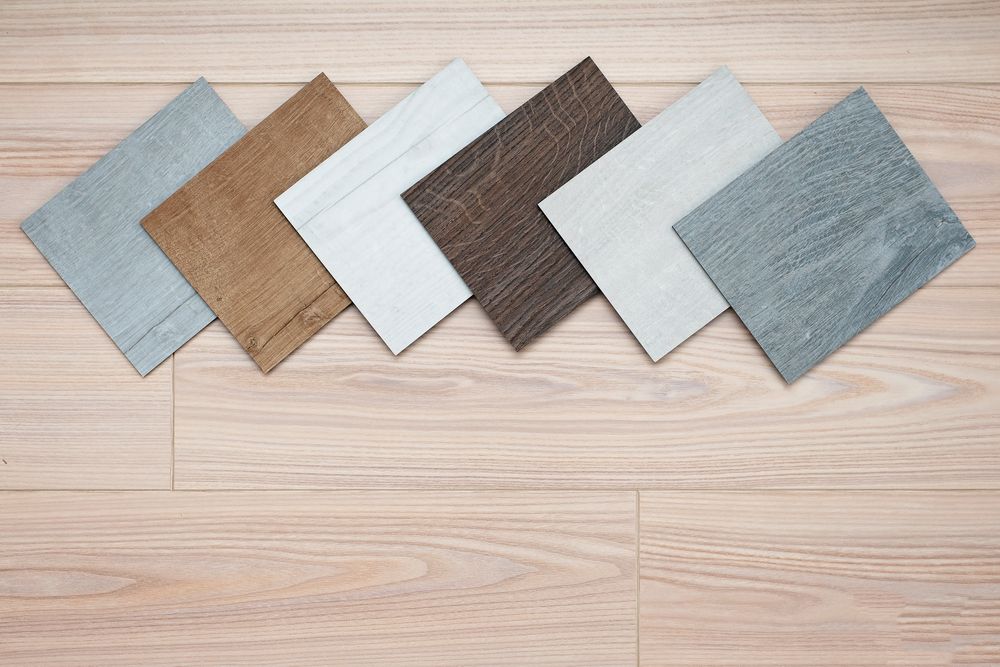 A selection of six square wood flooring samples of varying colours arranged on a light wood floor.