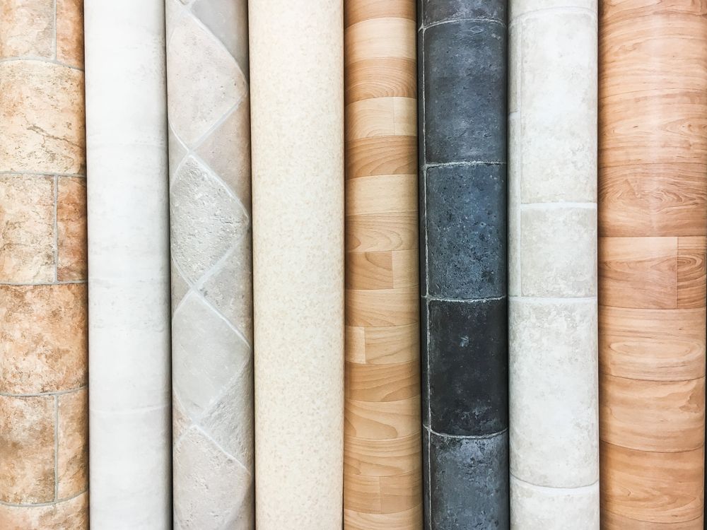 Rolled-up vinyl flooring samples in various colours and patterns, including wood grain and stone textures. Displayed vertically.