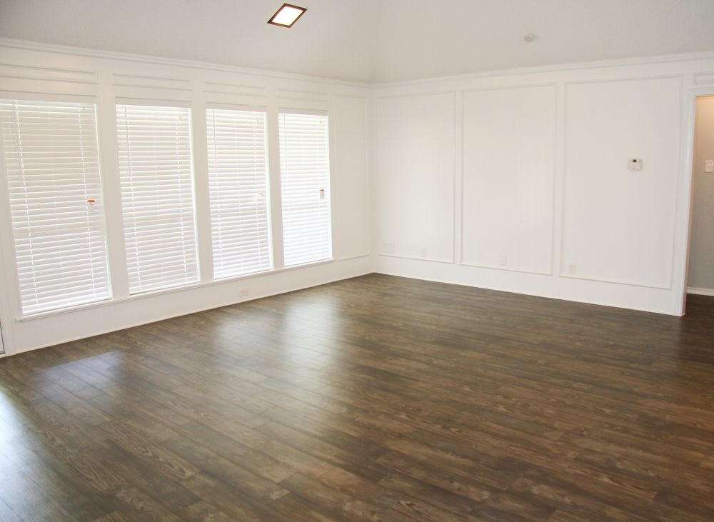 Empty room with dark hardwood floors, white walls and trim, and large windows with blinds.