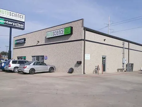 A car is parked in front of a building that says auto science enterprise.