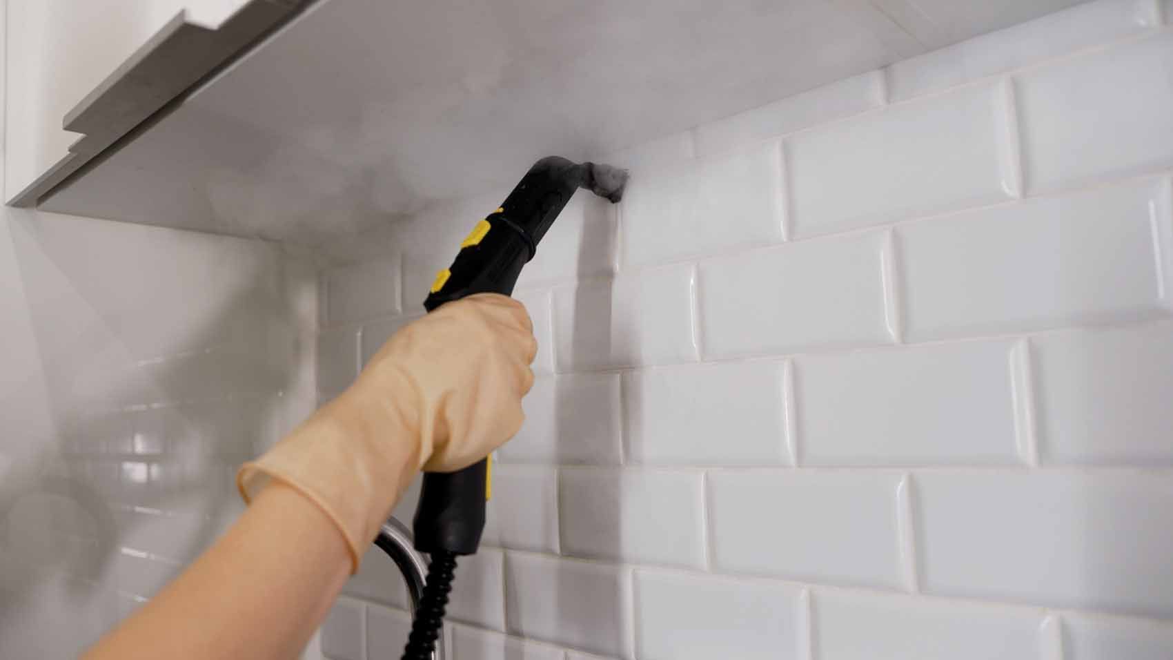 A person is cleaning a kitchen wall with a steam cleaner.