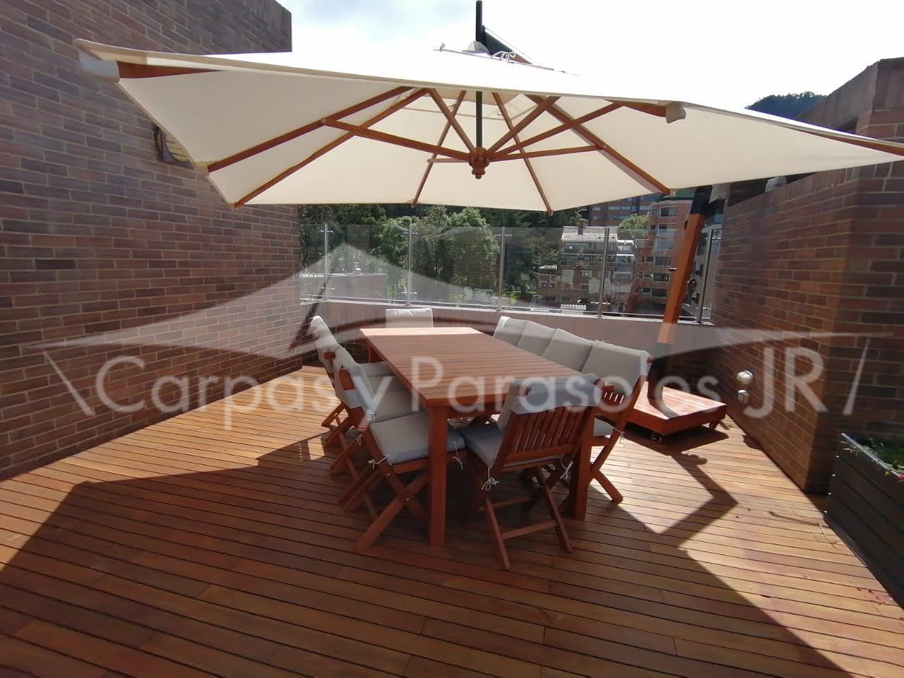 Un conjunto de muebles de patio con una mesa y sillas de madera a la sombra de una gran sombrilla beige