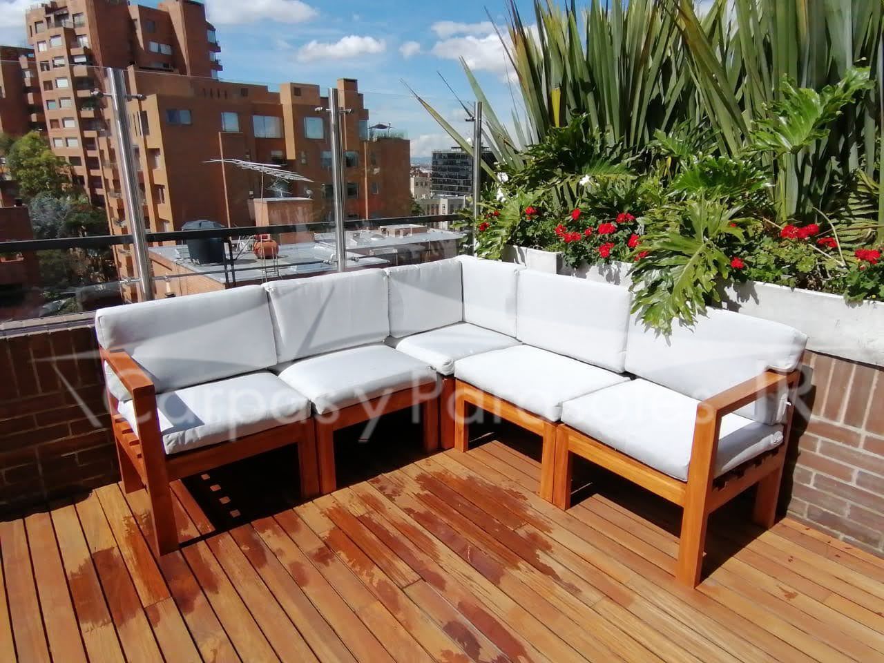 Sofá seccional de madera en forma de L para exteriores con cojines blancos sobre una terraza de madera con listones