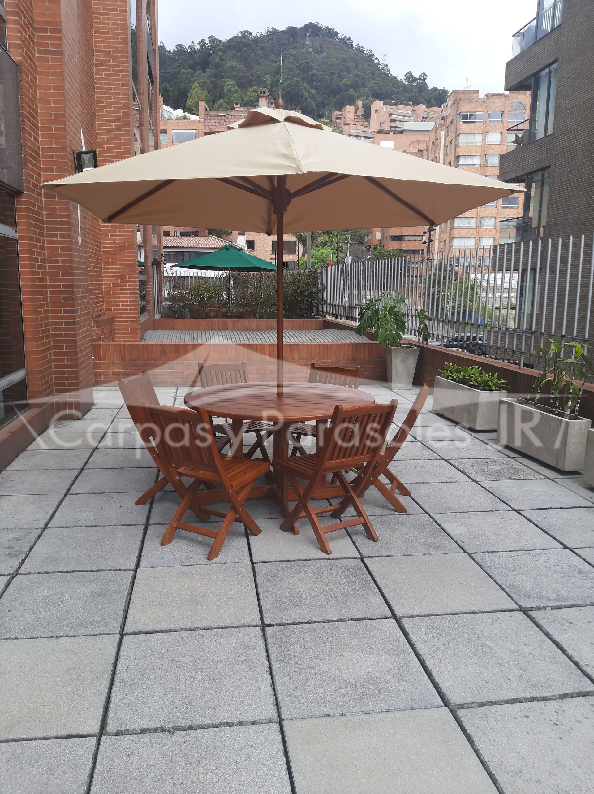 Un conjunto de comedor de madera para exteriores con una gran sombrilla beige en una terraza con suelo de baldosas