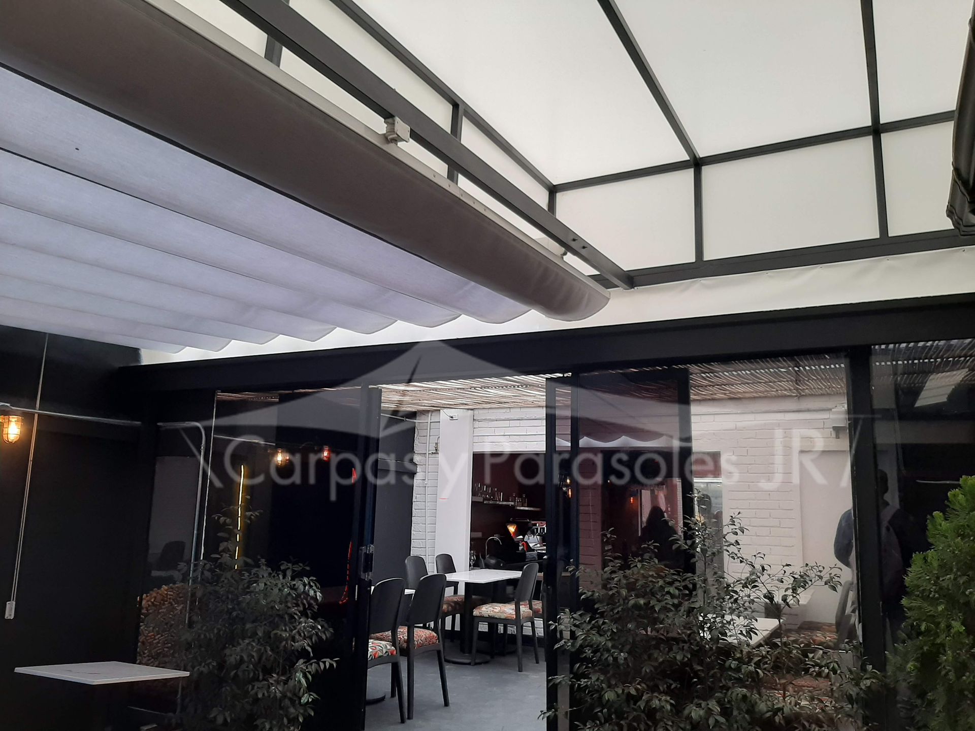 Un patio exterior con un toldo retráctil de tela, puertas plegables de cristal y muebles de comedor bajo una pérgola.