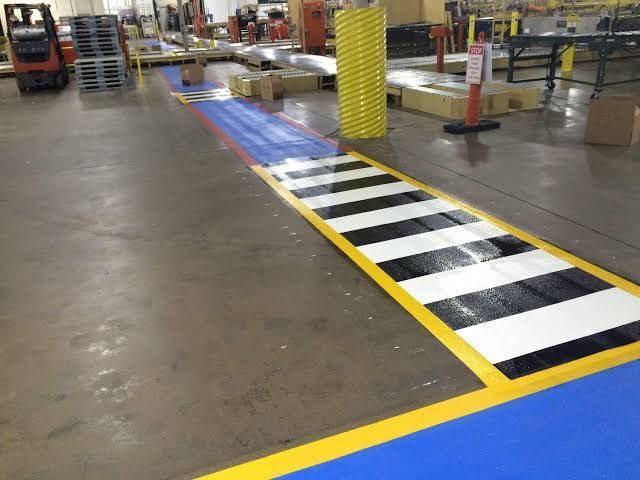 Indoor warehouse aisle with a black-and-white striped walkway outlined in yellow paint
