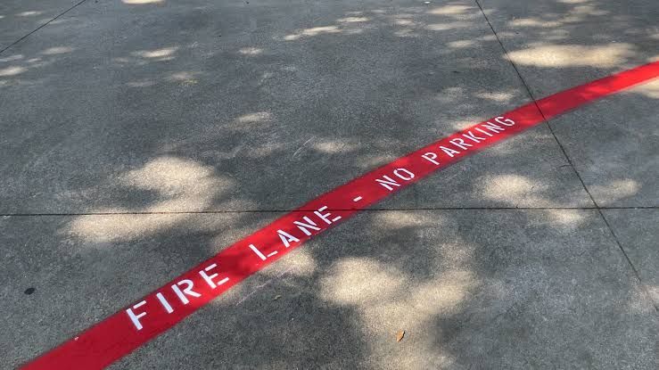 Red curb stripe labeled “FIRE LANE – NO PARKING” on a concrete sidewalk.