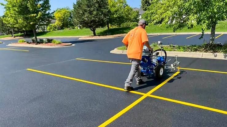 Worker painting yellow lines on a blacktop parking lot with a line-marking machine