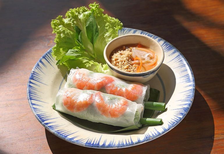 Fresh shrimp spring rolls on a plate with dipping sauce, herbs, and chopsticks on a wooden table