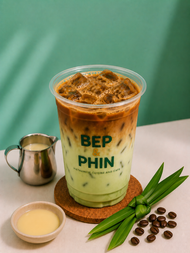 Iced Vietnamese coffee in a glass with foam and star anise on top, lit by warm sunlight.