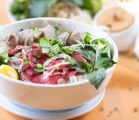 Bowl of beef noodle soup topped with green onions and sliced meat