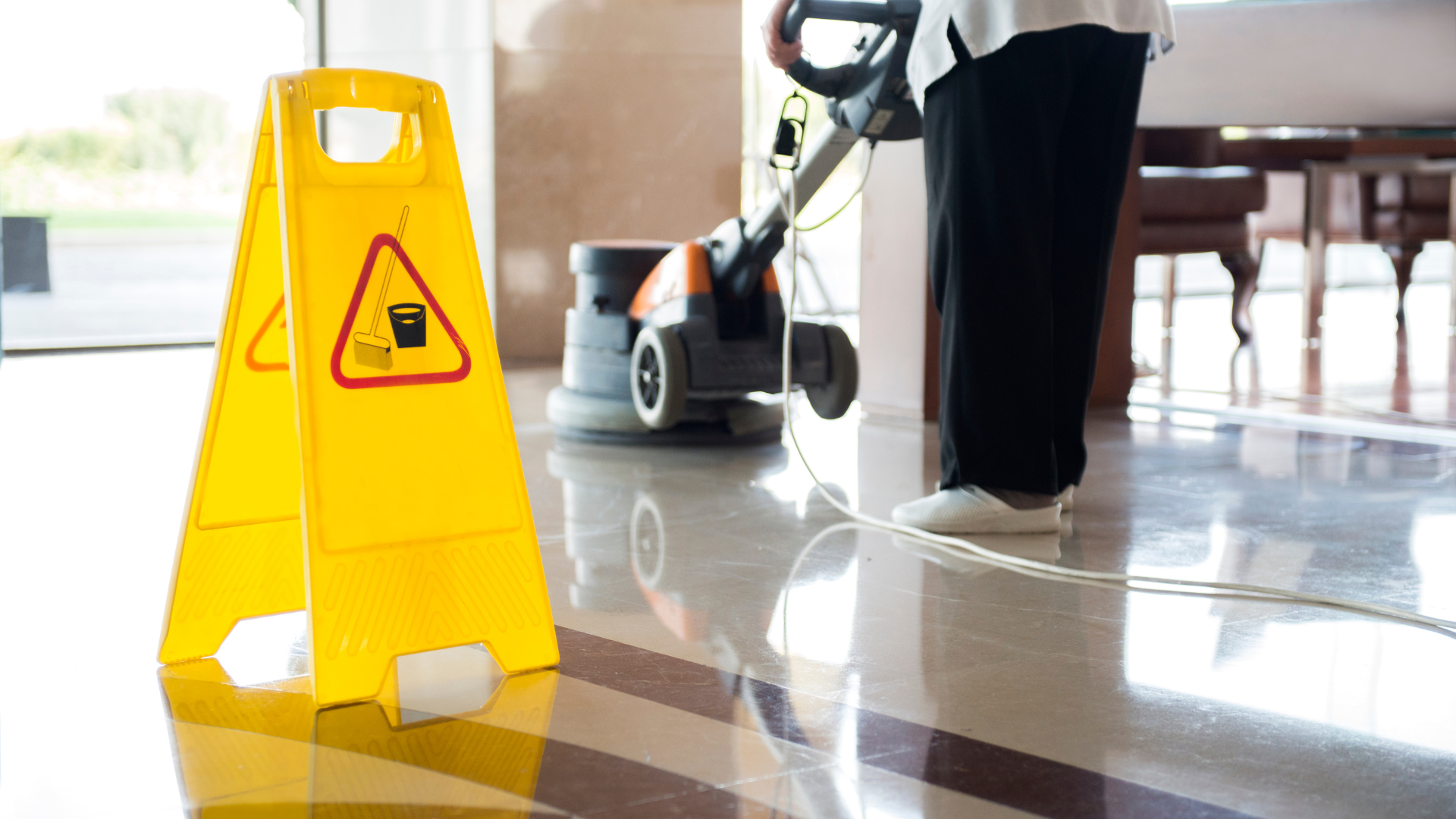 A person is cleaning a floor next to a yellow caution sign.