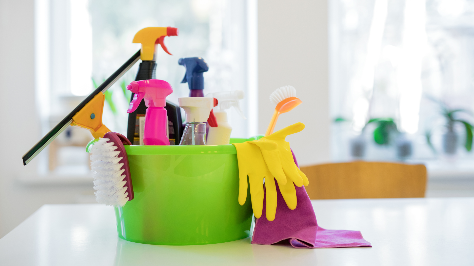 A green bucket filled with cleaning supplies on a table.
