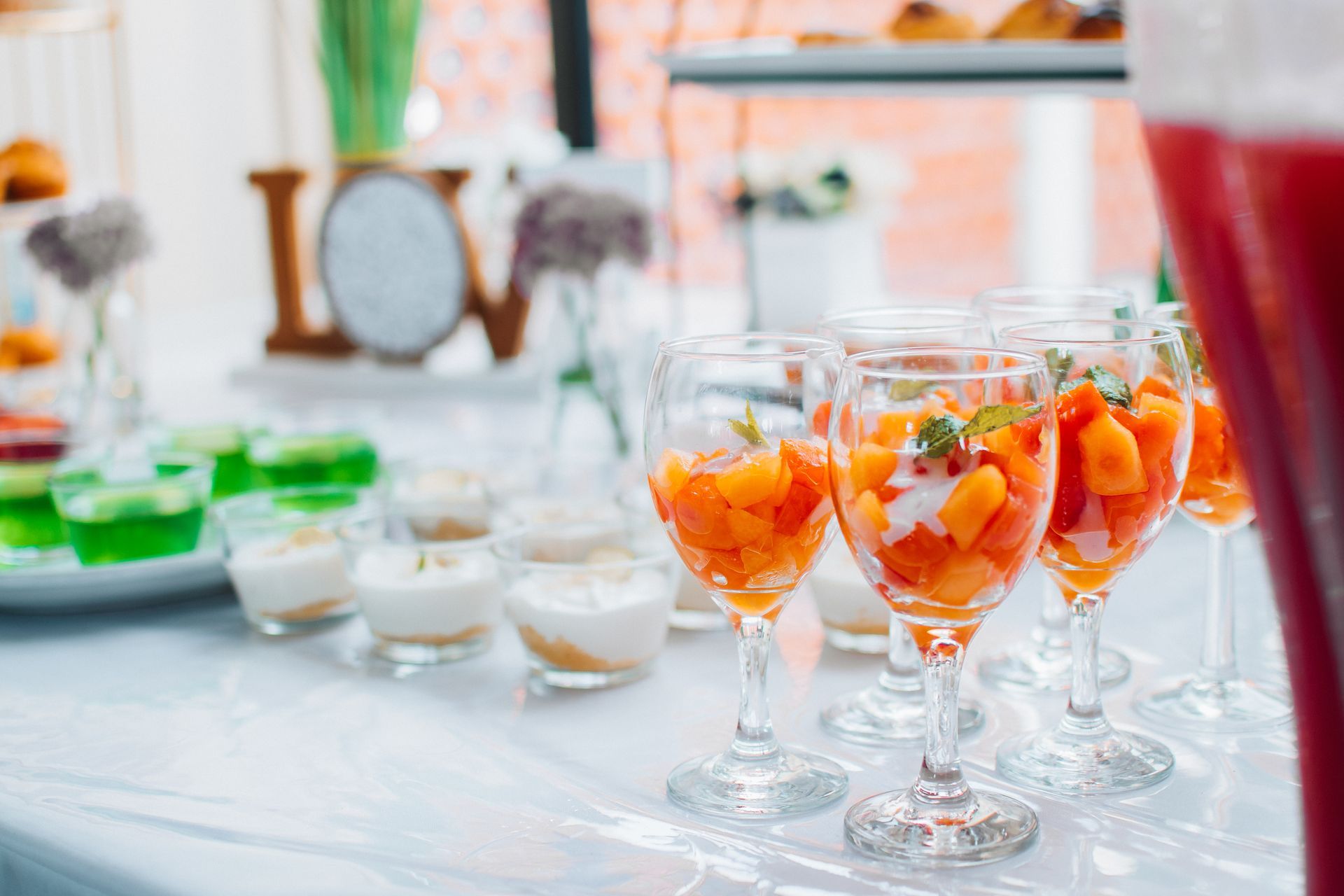 Mesa de postres con copas de vino llenas de fruta, junto con otras delicias y un cartel de 