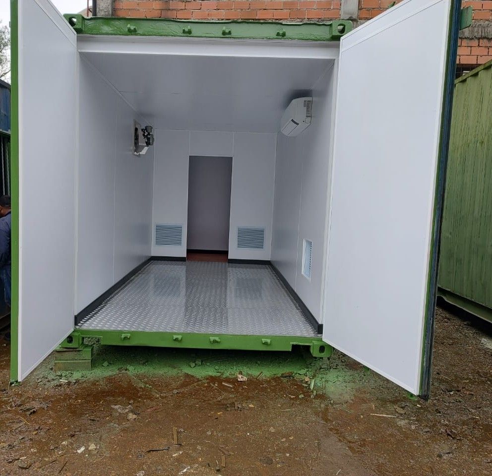 Habitación diáfana, construida con un contenedor blanco, con puertas dobles, suelo metálico y una pequeña puerta trasera.