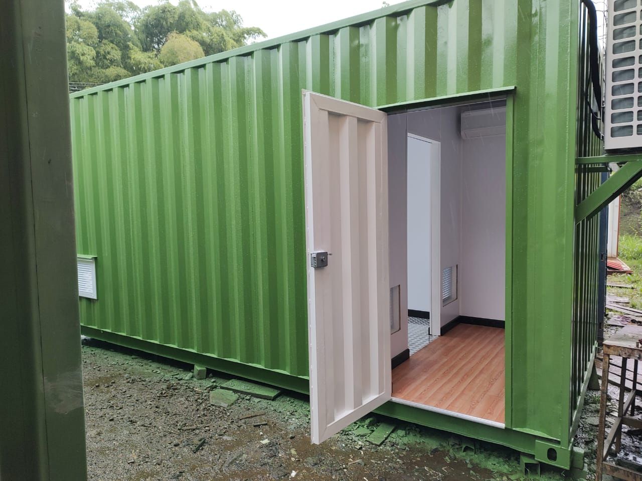 Contenedor de transporte verde con la puerta abierta, que deja ver una pequeña habitación interior con suelo de madera.