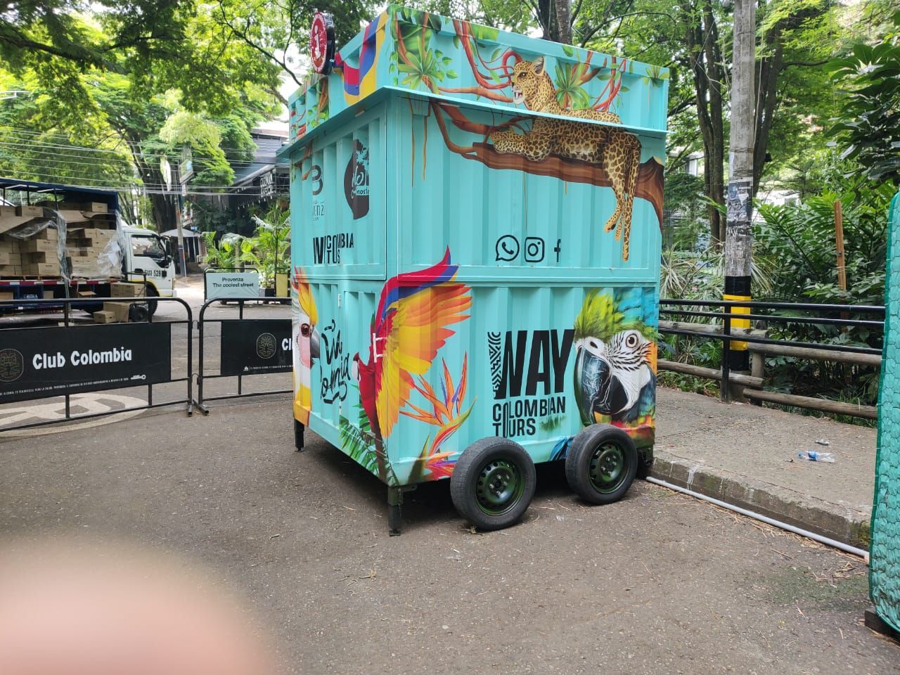 Un pequeño carrito colorido con grafitis estacionado en un sendero arbolado junto a una puerta.