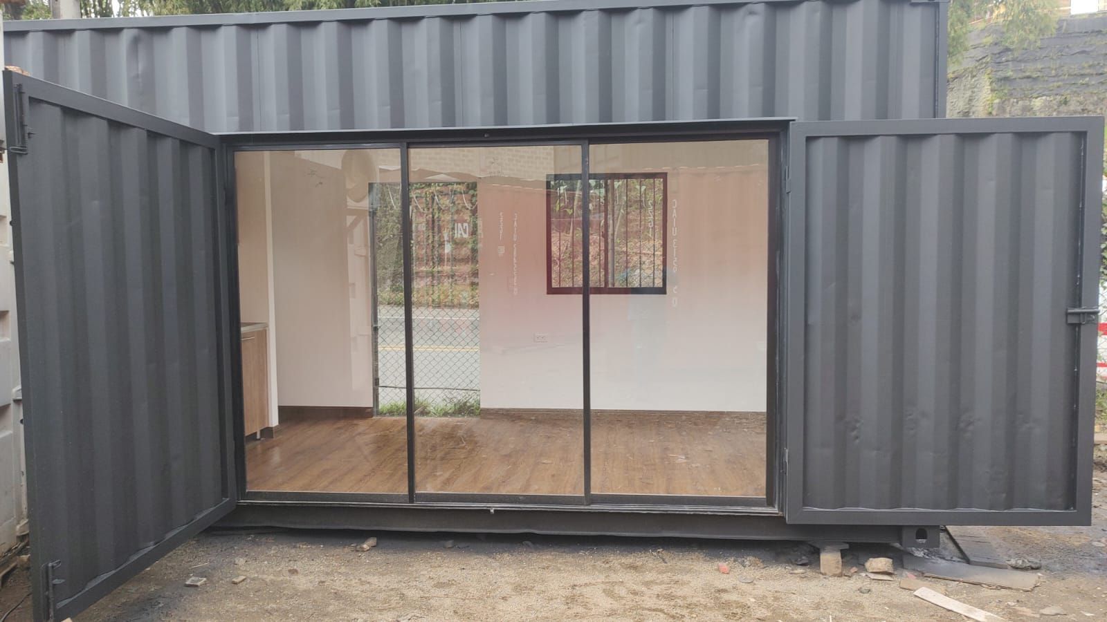 Contenedor de transporte abierto utilizado como una pequeña habitación, con puertas dobles de cristal