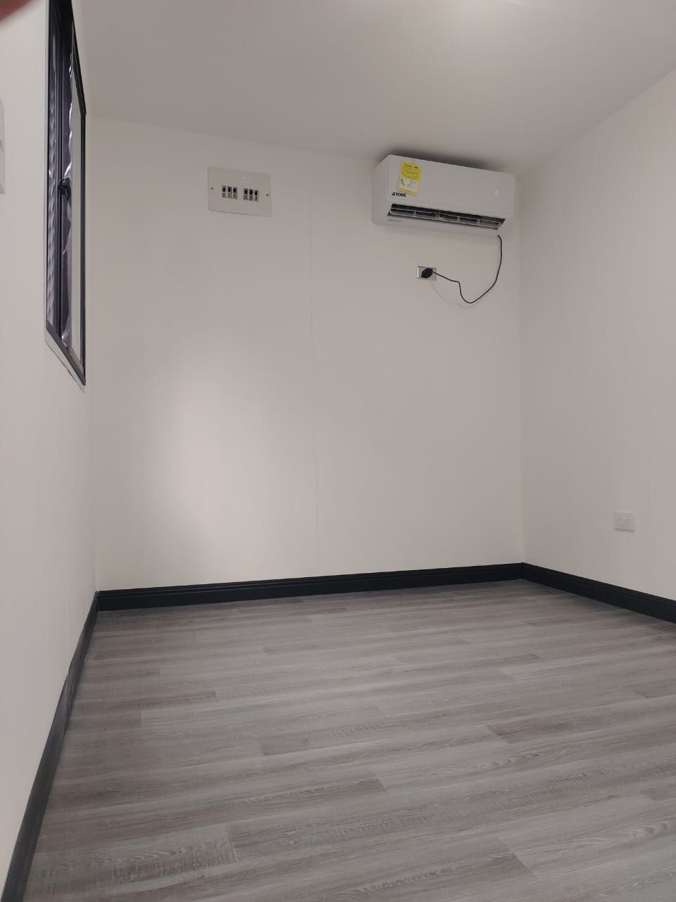 Habitación vacía con paredes blancas, suelo de imitación madera gris y aire acondicionado montado en la pared.