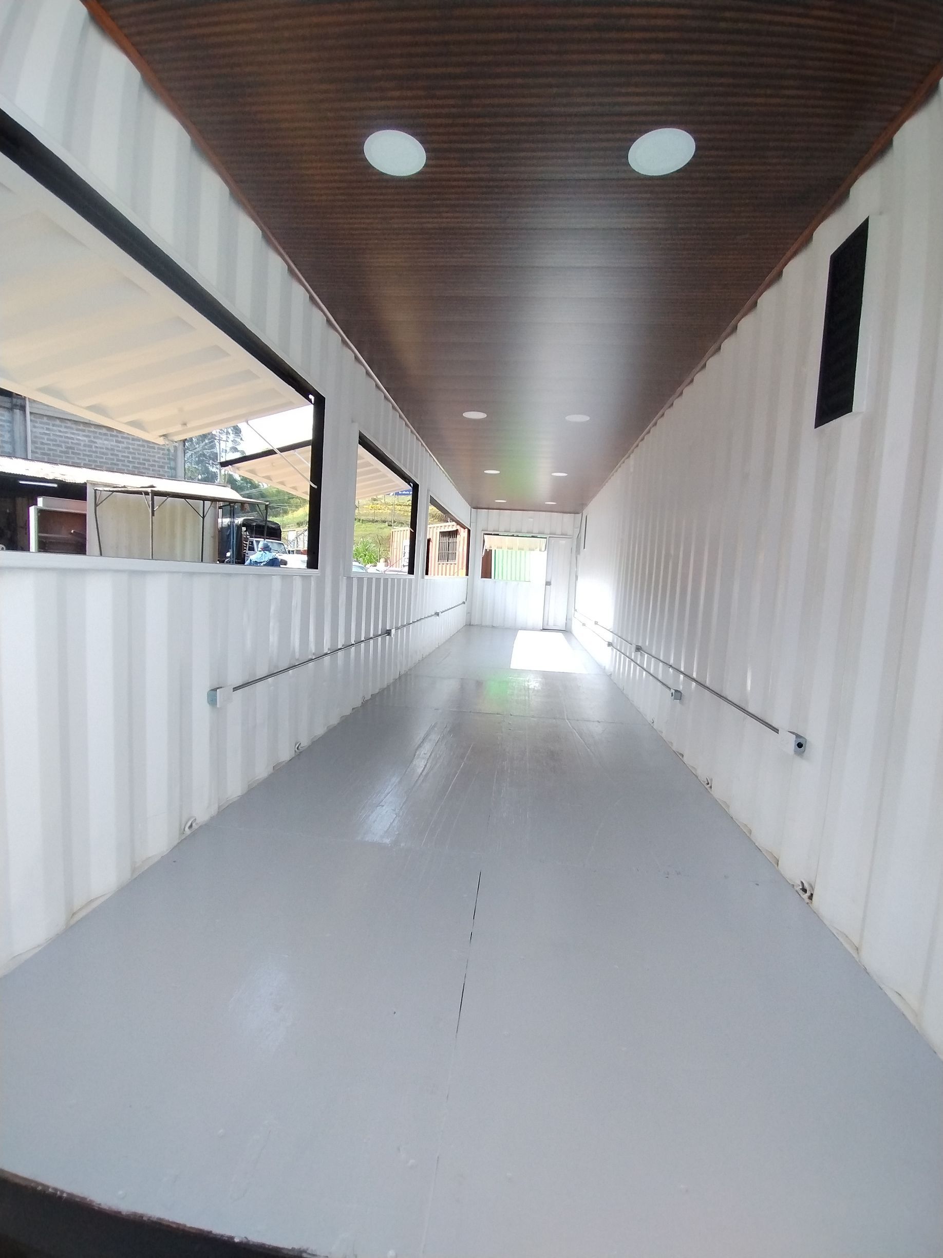 Largo pasillo blanco con suelo brillante, techo de madera y ventanas a lo largo del lado izquierdo.