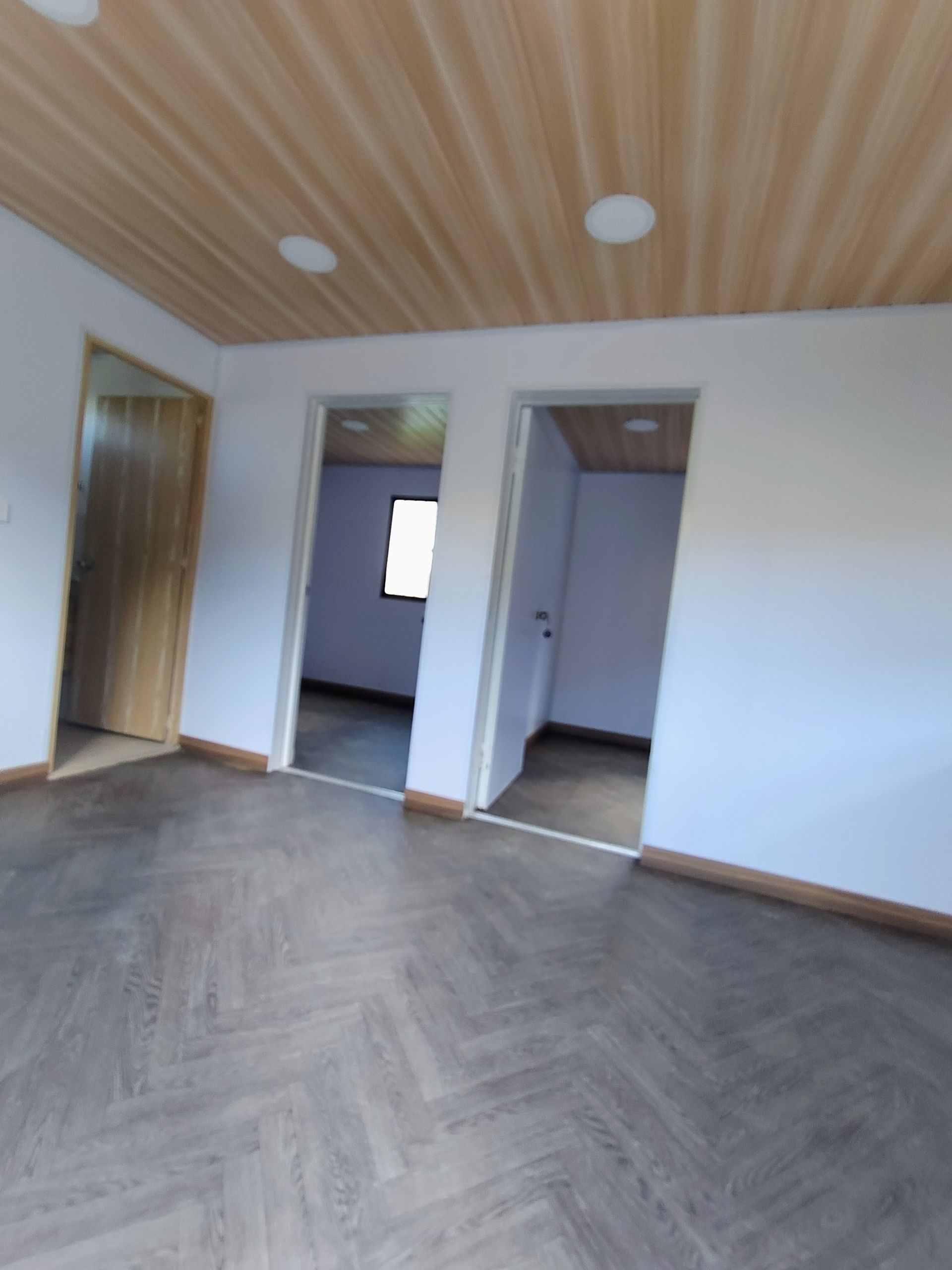 Habitación moderna vacía con techo de madera, suelo de espiga y puertas abiertas.