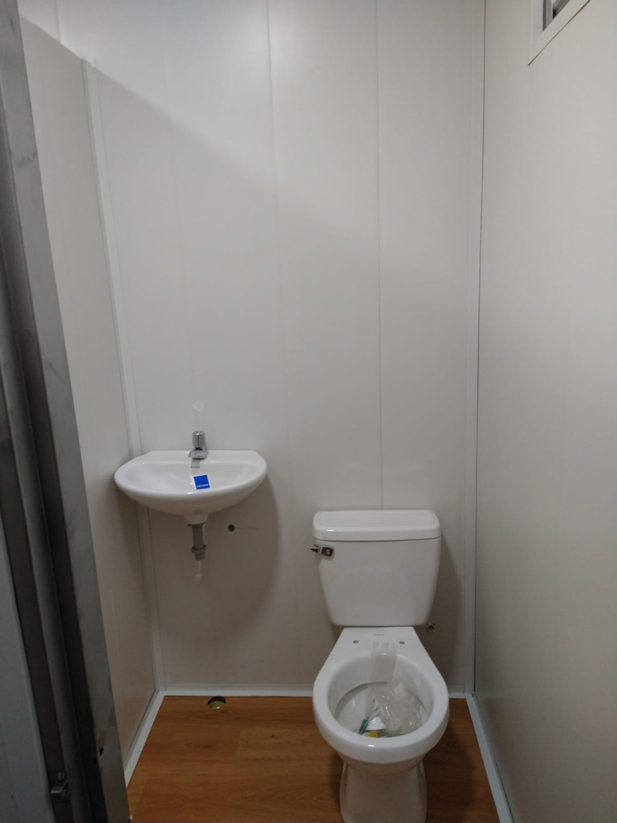 Baño pequeño con inodoro, lavabo mural y revestimiento de suelo con aspecto de madera.