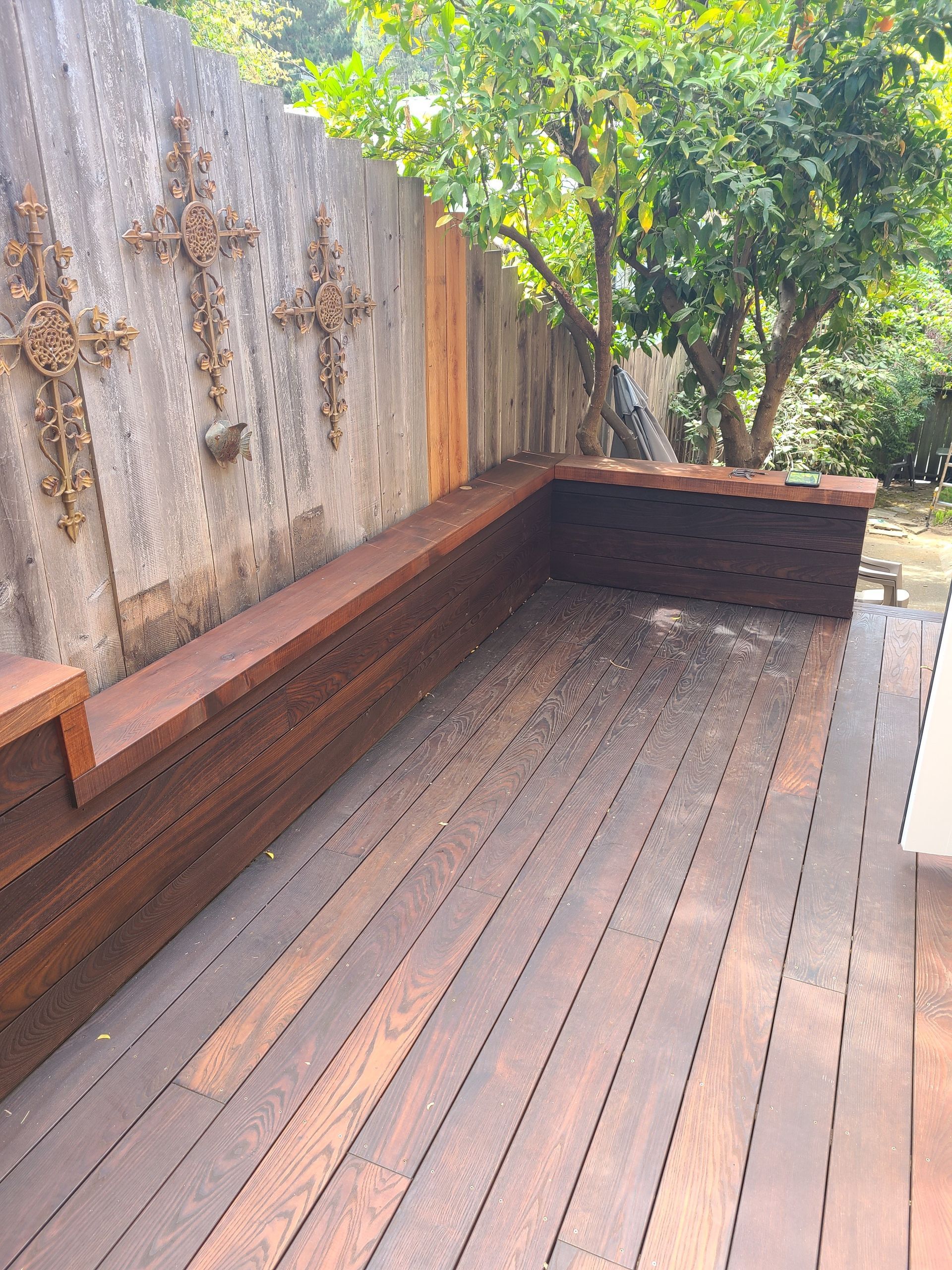 A wooden deck with a bench and a fence in the background.