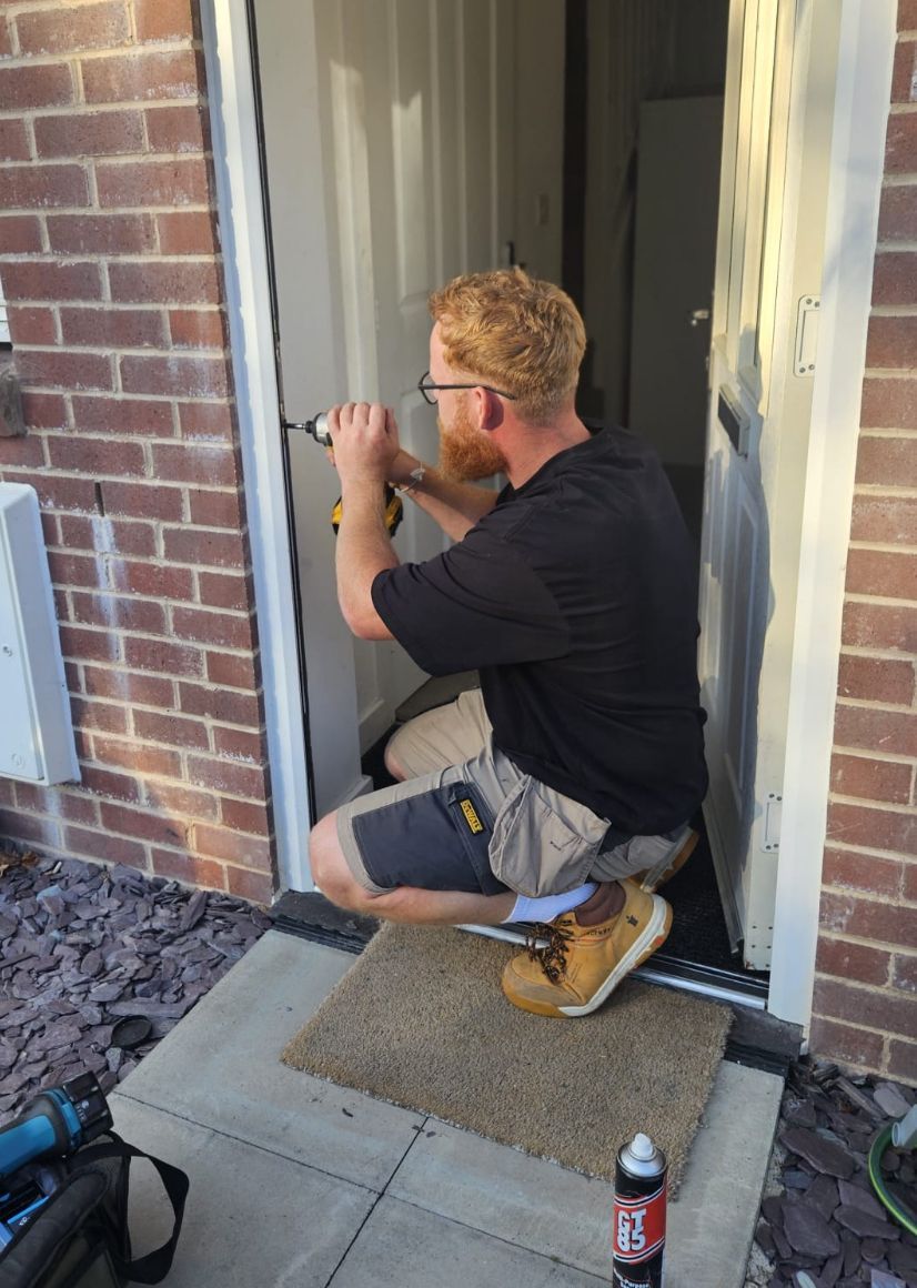 A man is kneeling down to fix a door lock.
