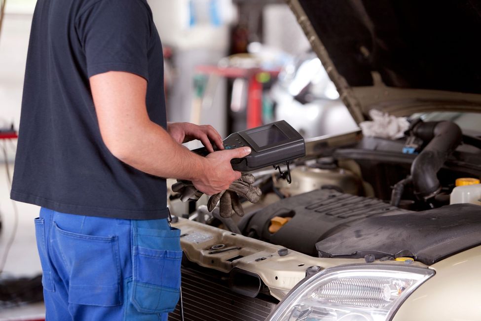 Mecánico utilizando una herramienta de diagnóstico en el motor de un automóvil con el capó abierto en un taller de reparación.