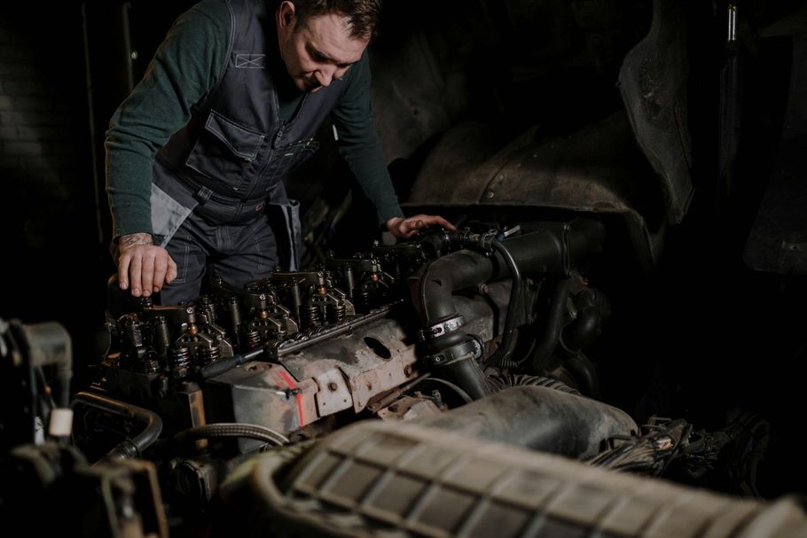 Hombre con ropa de trabajo oscura inspeccionando un motor grande en un entorno industrial con poca luz.