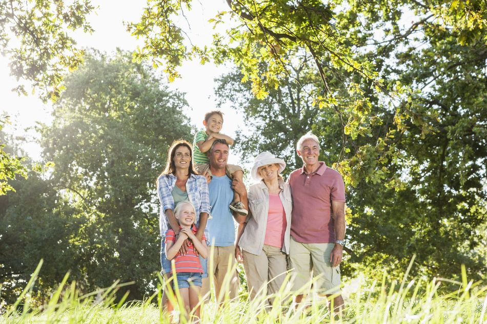 Family standing together outdoors in a sunny green field, smiling under trees